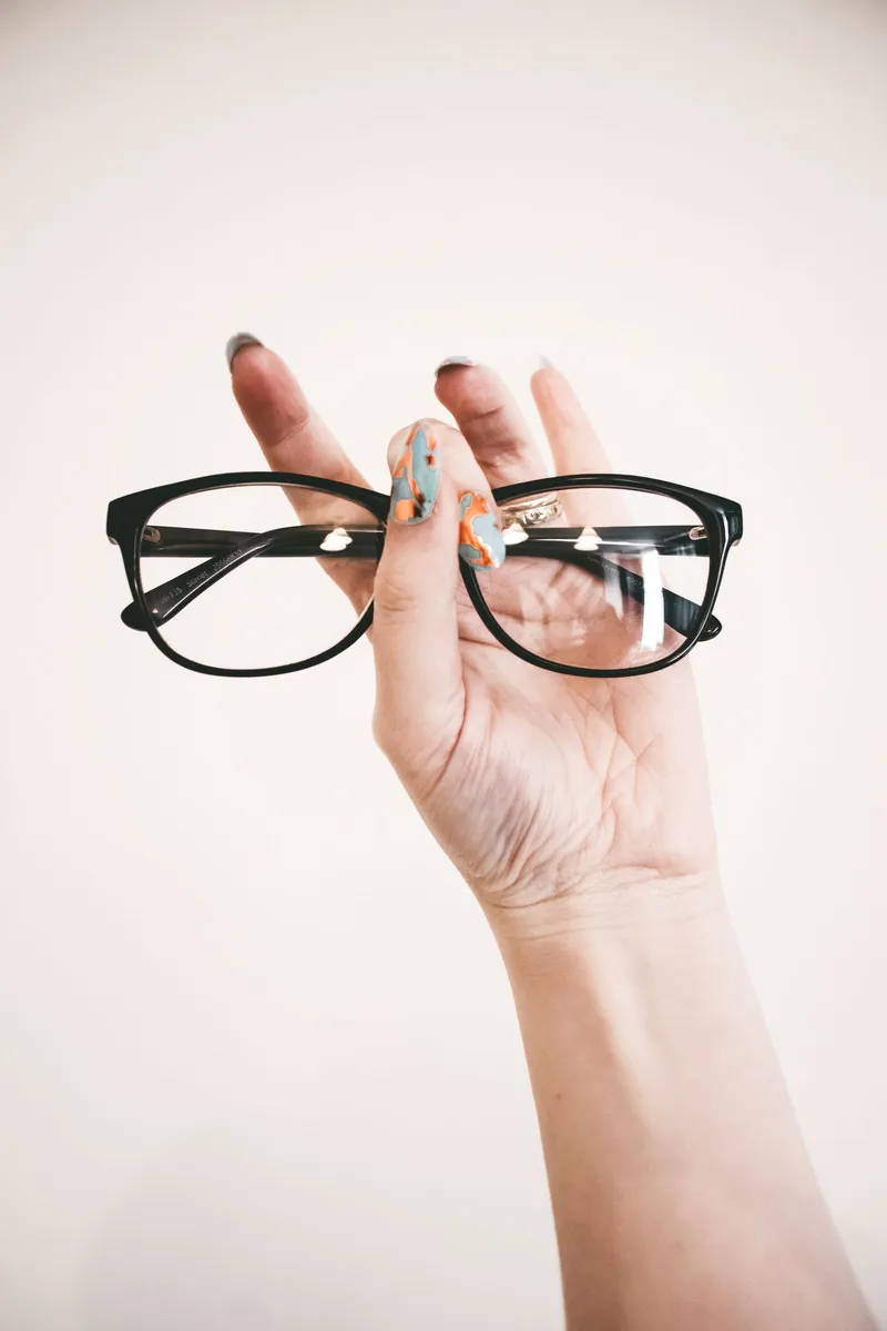 Una mano sostiene unas gafas graduadas modernas sobre fondo claro
