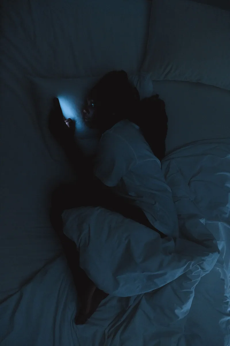 Mujer usando el móvil en la cama en una habitación a oscuras antes de dormir